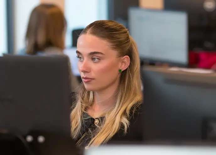 A young woman with a serious expression looking at a computer screen in a modern office.